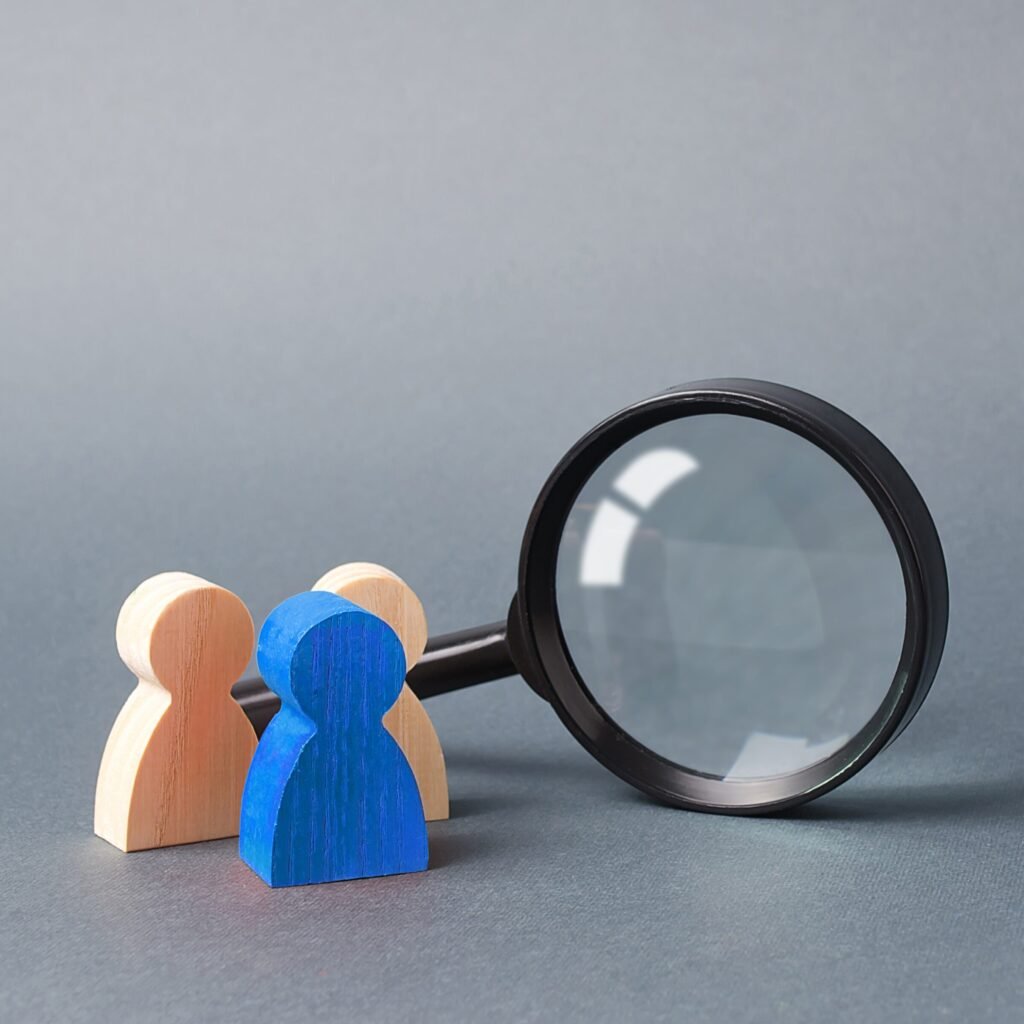 three wooden human figure stands near a magnifying glass on a gray background. search for vacancies and work. human resources, management. the concept of the search for people and workers.